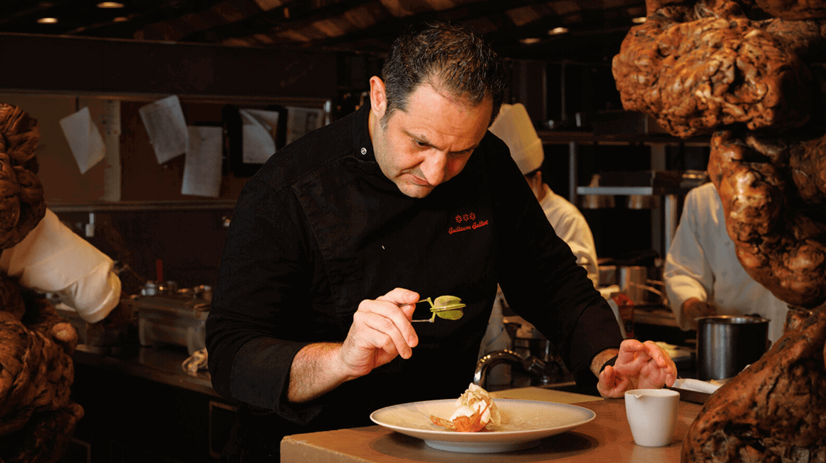 Chef carefully plating a fine-dining dish in a professional restaurant kitchen.