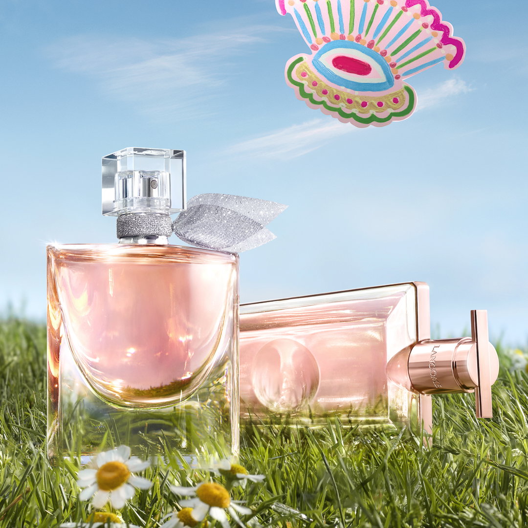 La vie est belle Eau de Parfum, mascara Idôle Flutter Extension e Rénergie H.C.F. Triple Serum Lancôme, fotografati su un prato fiorito in un'atmosfera primaverile.