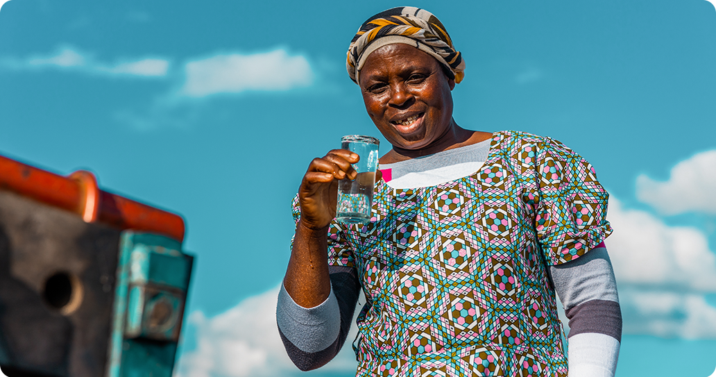 A woman smiling at the camera as she holds a glass of clean water.
