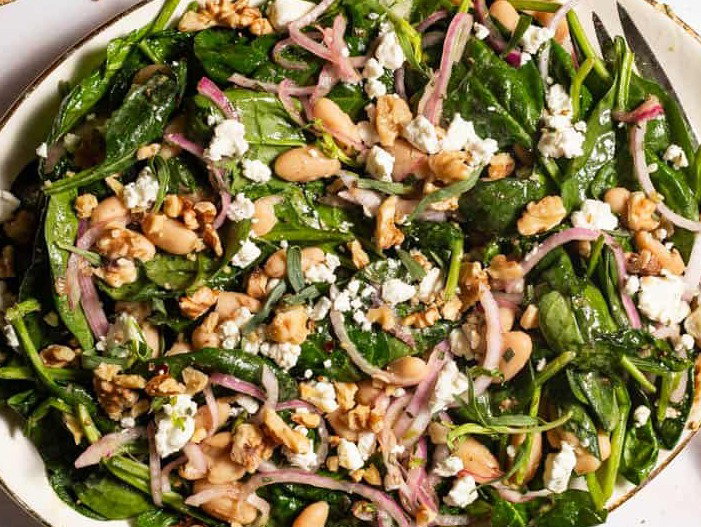 Wilted spinach salad on a platter with a serving fork.