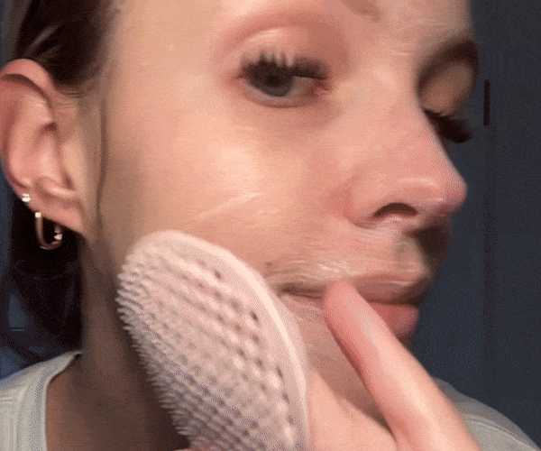 Animated GIF of a woman using a pink silicone cleansing brush to apply cleanser to her cheek