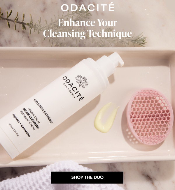 Odacité Edelweiss Extrême Hydra-Calm Cream Cleanser lying on a ceramic tray beside a pink silicone cleansing brush and a drop of product, with the text "Enhance Your Cleansing Technique" and a Shop the Duo button