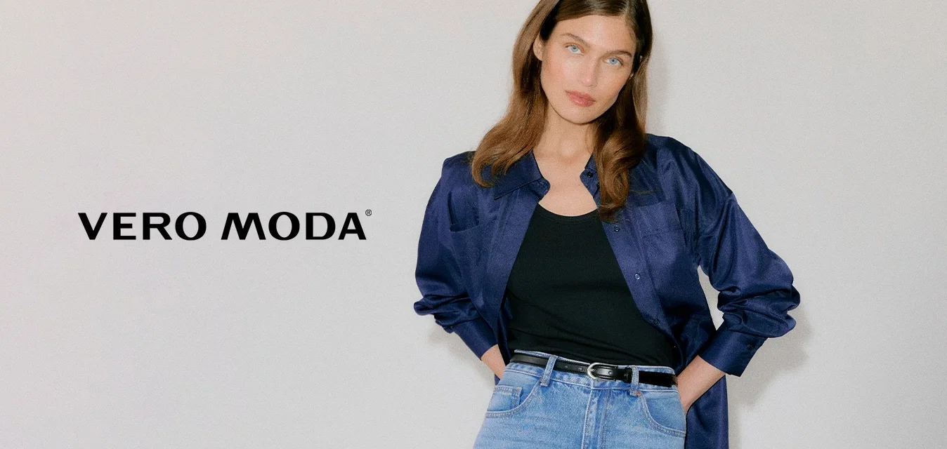 Jeune femme portant une chemise en satin bleu foncé sur un débardeur noir, un jean taille haute bleu clair et des talons pointus noirs à œillets.