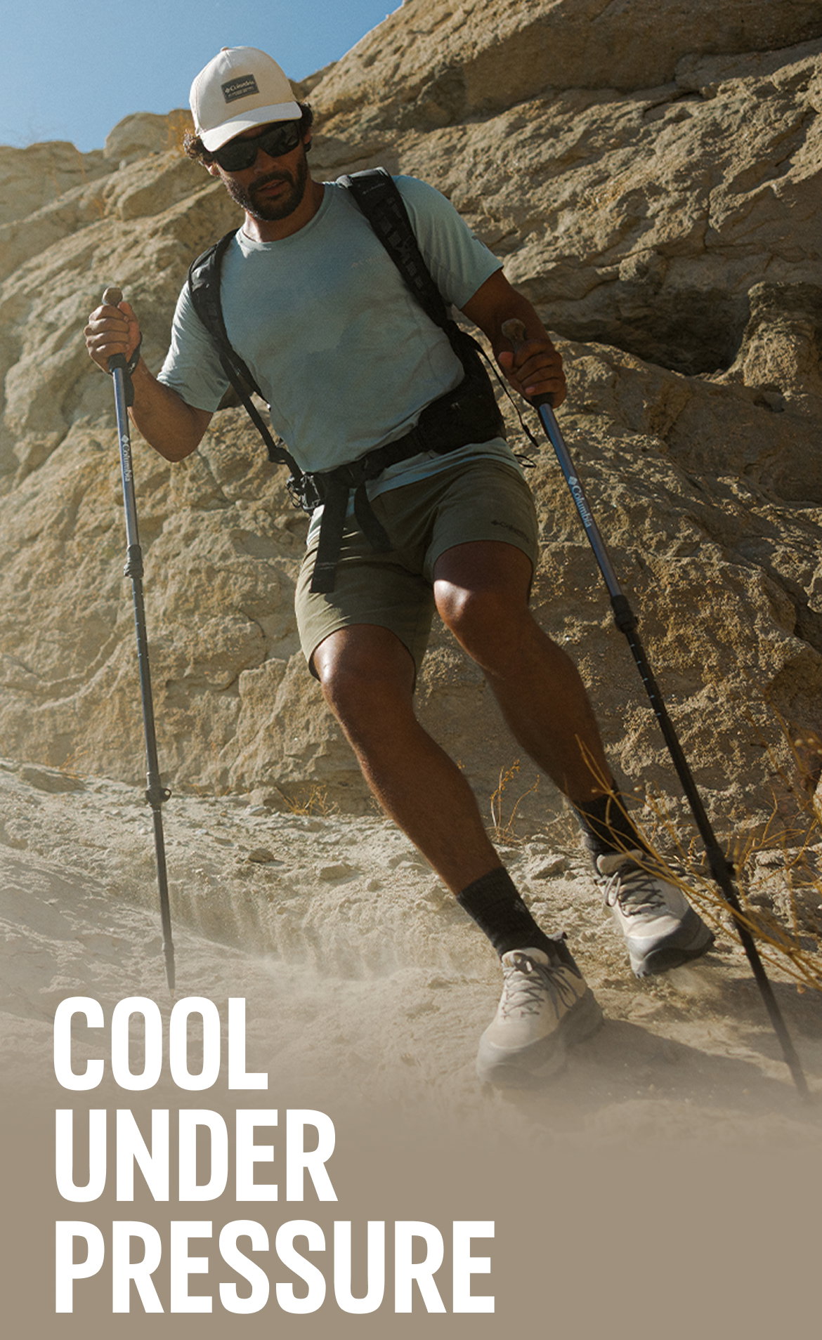 A man carefully hiking down a steep rocky hill with hiking poles. 