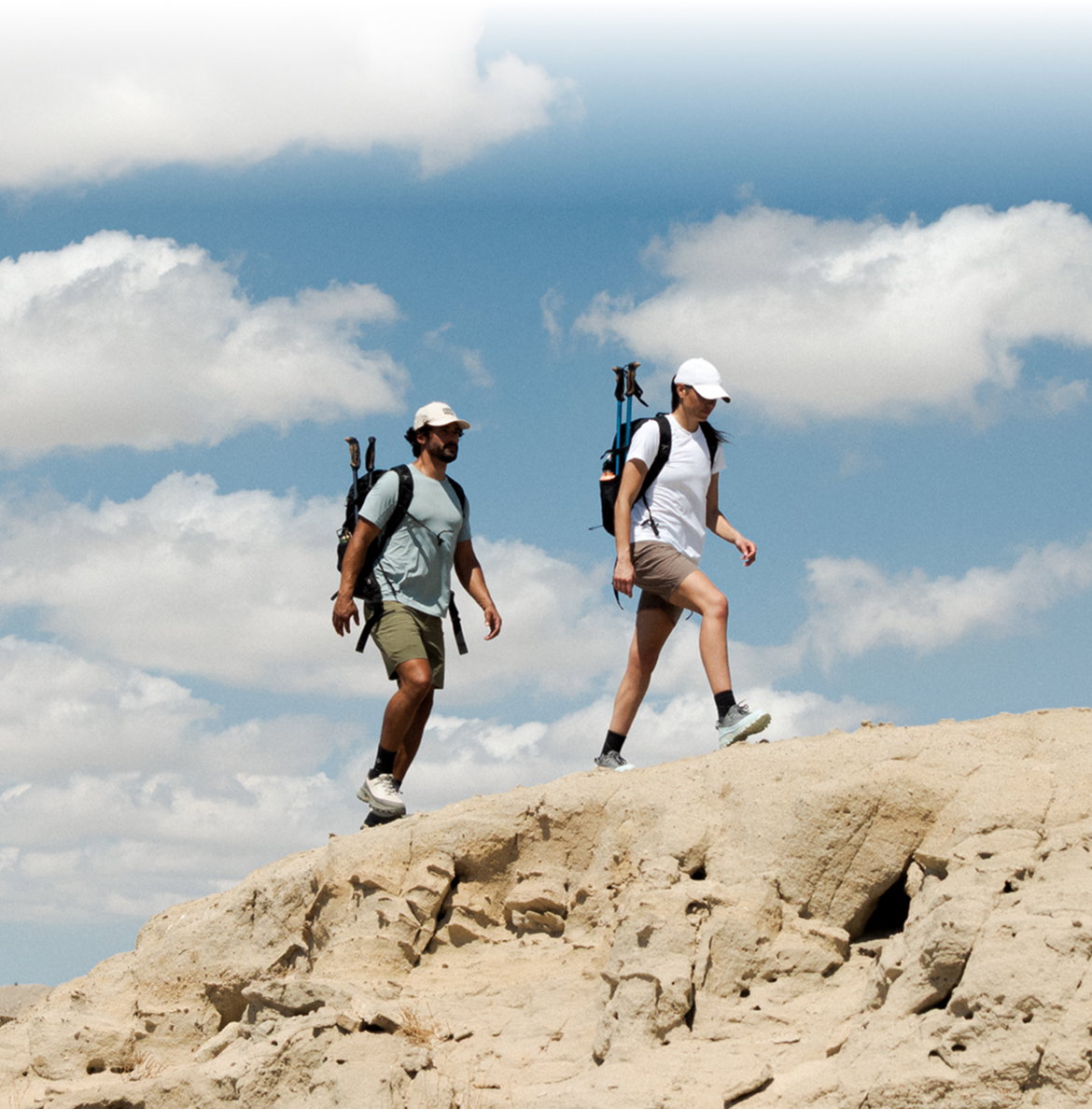 An image of a woman and a man backpacking a dry, rocky terrain on a hot and sunny day.
