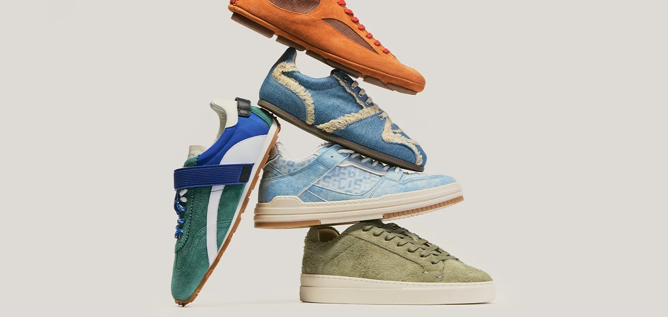 Pila de cinco zapatillas casuales en estilos naranja, azul, verde y vaquero, dispuestas contra un fondo claro y liso.