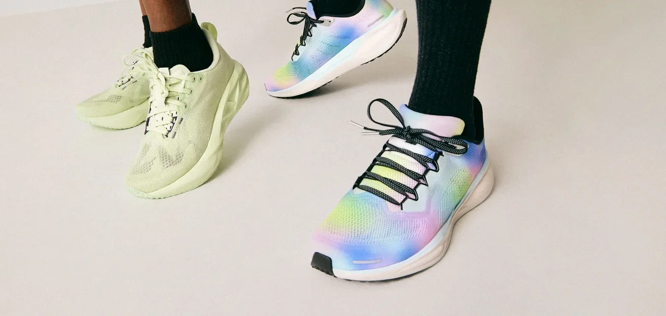 Dos personas que llevan calcetines negros y zapatillas deportivas coloridas, de pie sobre un suelo de color claro, frente a un fondo sencillo.