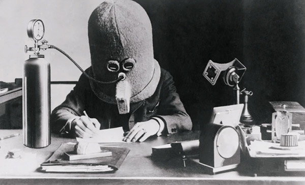 Black-and-white photo of a person wearing Hugo Gernsbach’s ‘isolator’ helmet while writing at a desk.