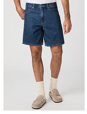 A man's legs wearing dark blue denim jean shorts paired with light tan loafers.
