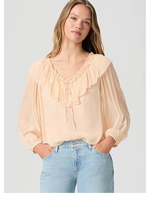 A woman wearing a peach flowy blouse and light wash denim blue jeans.