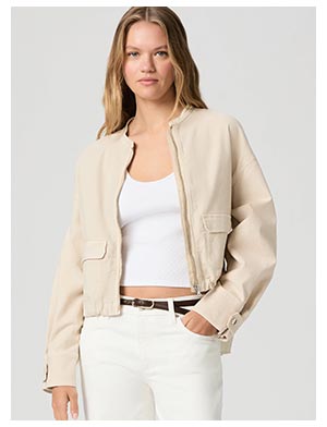 A woman wearing a beige jacket, white tank and cream denim jeans.