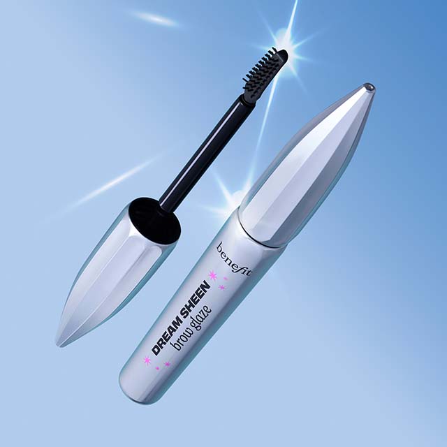 A silver eyebrow gel tube with a mascara wand next to it, set against a blue background with star-like reflections.