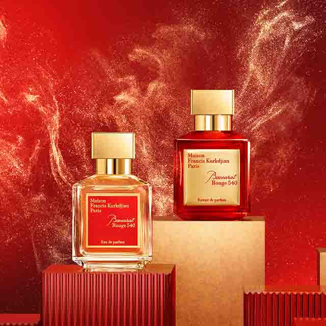 Three bottles of Maison Francis Kurkdjian Baccarat Rouge 540 perfume are displayed on red and gold platforms with a fiery background.