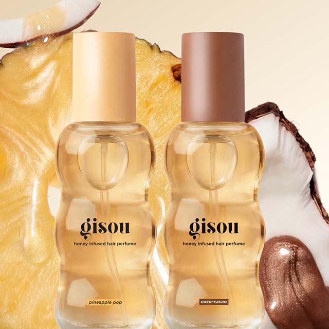 Two bottles of Gisou honey-infused hair perfume, 'Pineapple Pop' and 'Coco-Cacao,' in front of pineapple and coconut slices.