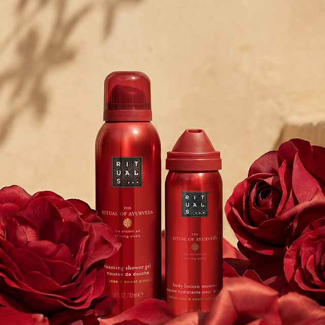 Red bottles of 'The Ritual of Ayurveda' products surrounded by red roses.