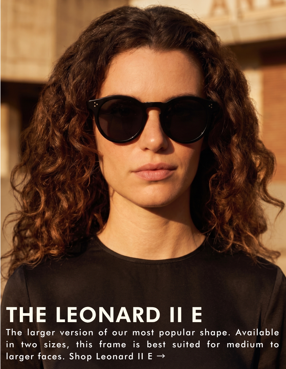A portrait of a woman with curly brown hair wearing the Leonard II E sunglasses in black. The lighting is warm, suggesting sunset. The text reads: 