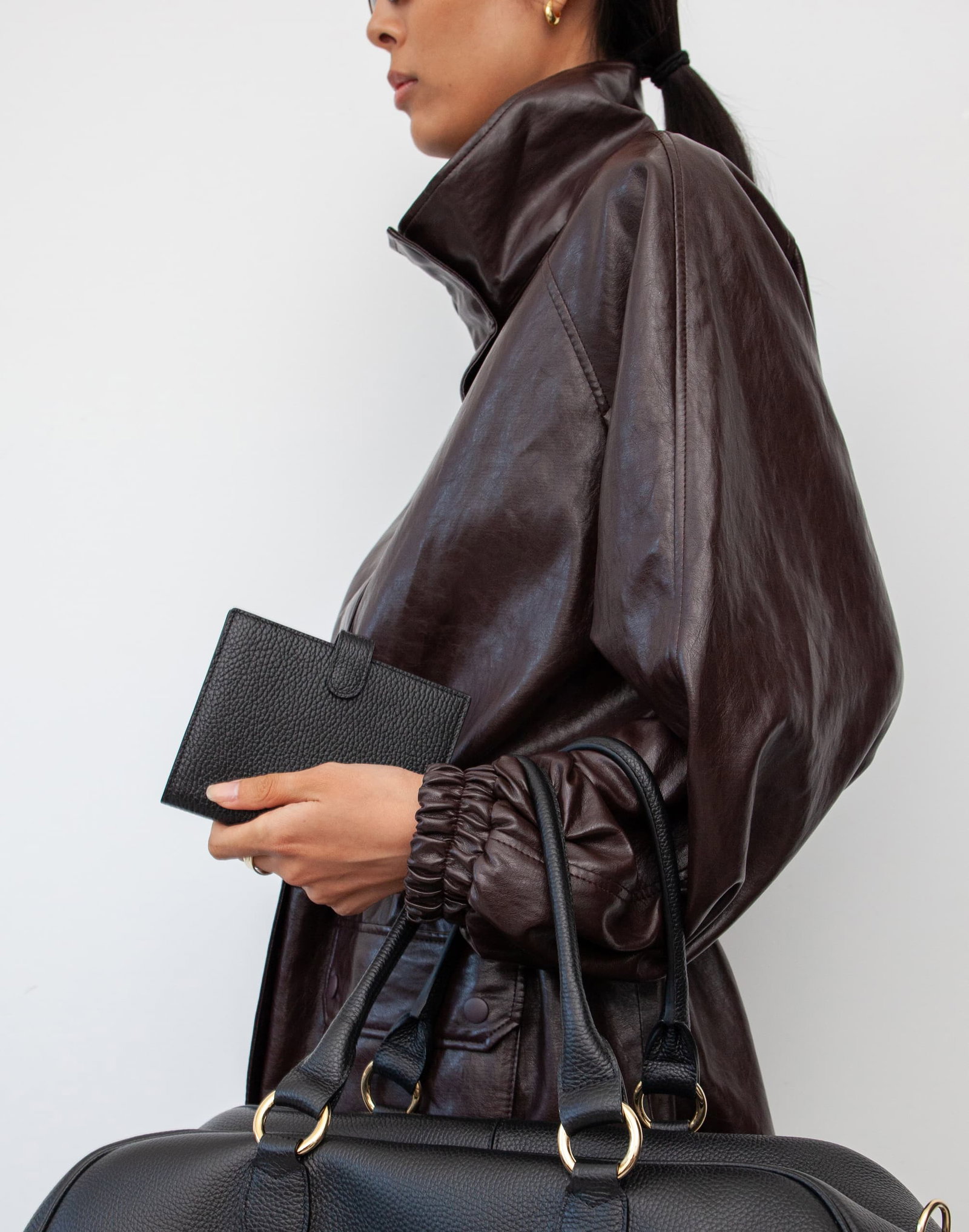 profile view of a model holding a black leather passport wallet with  a weekender resting on her forearm