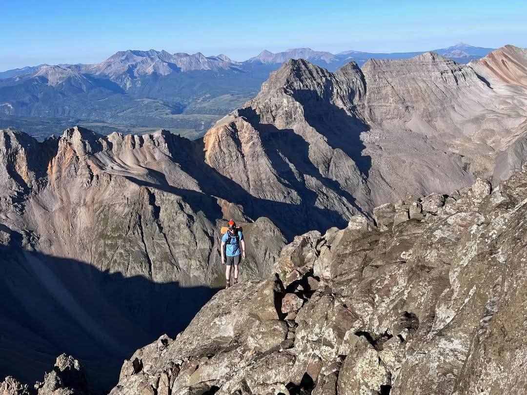 Hiker standing on edge of ridgeline with mountains behind