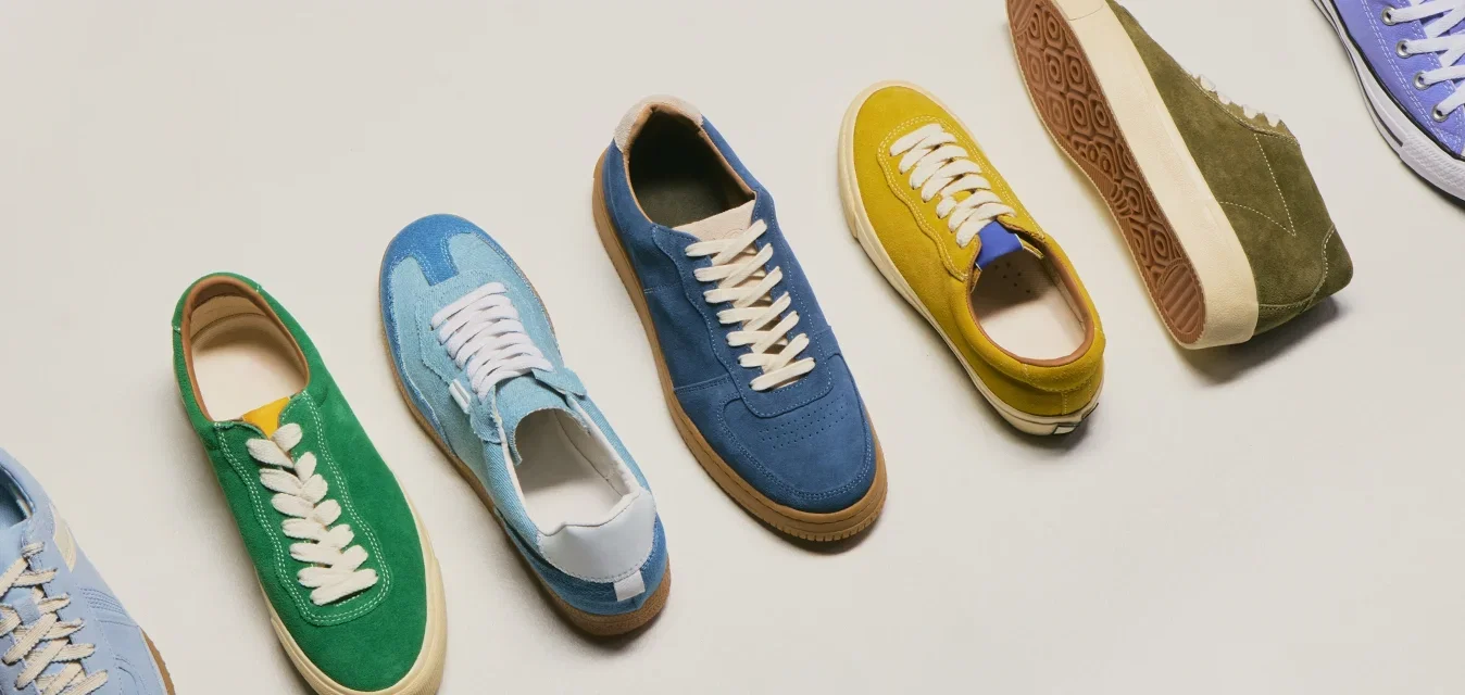 Siete zapatillas casuales de ante en varios colores, incluyendo azul, verde, amarillo y morado, dispuestas en fila sobre un fondo claro.