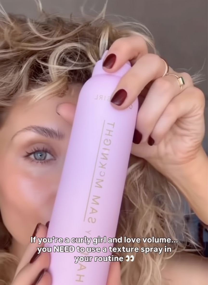 A woman holds a pink spray bottle near her curly hair, with text about texture spray.
