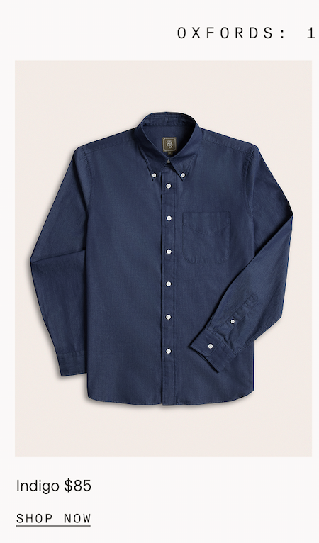 Flat lay of a solid indigo button-down Oxford shirt with a button-down collar and a single chest pocket. Partial header text reads: "OXFORDS: 1." Below the image: "Indigo $85." CTA: "SHOP NOW"