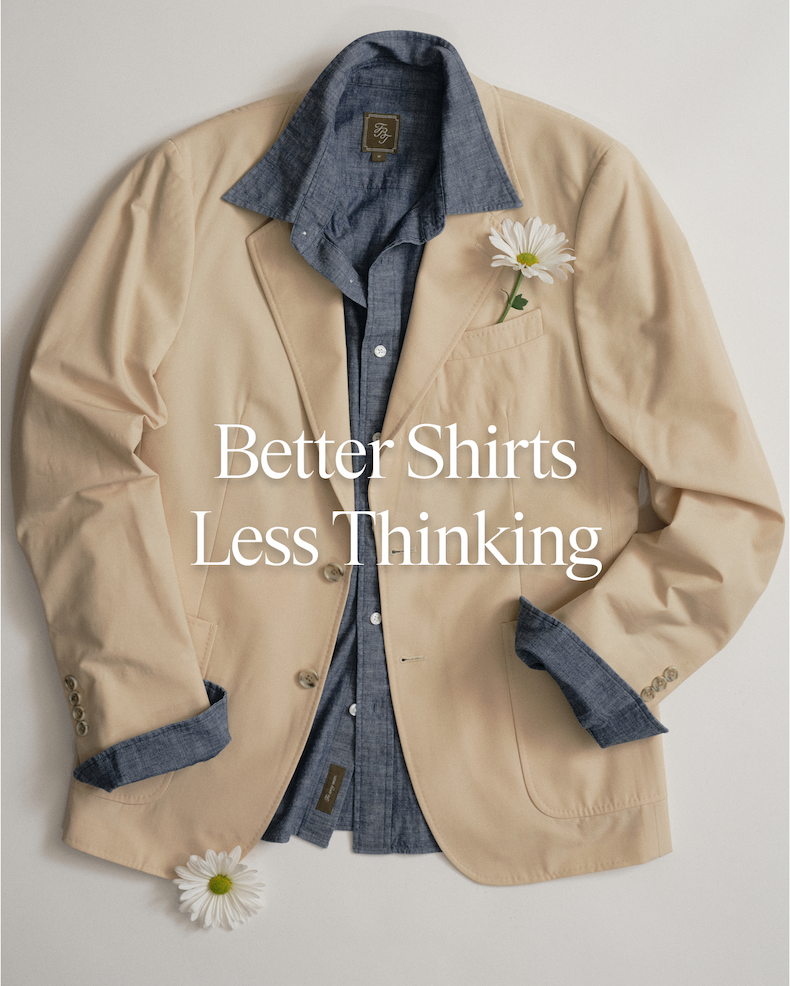 Overhead flat lay of a tan sport coat layered over a blue chambray shirt, with two white daisy flowers as styling accents. Text overlay reads: "Better Shirts Less Thinking"