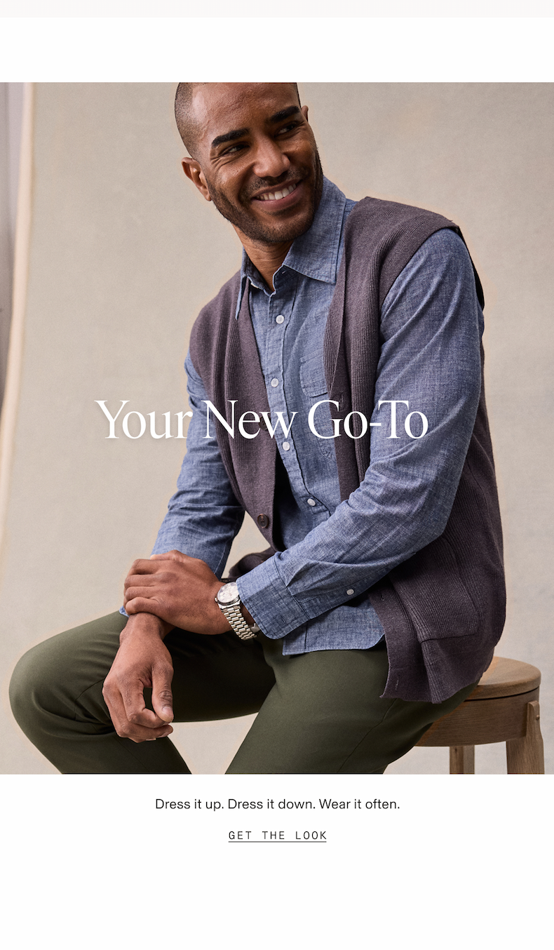 Man smiling and seated on a wooden stool, wearing a blue chambray shirt layered under a dark gray knit vest with olive chinos and a watch. Text overlay reads: "Your New Go-To." Below the image: "Dress it up. Dress it down. Wear it often." CTA: "GET THE LOOK"