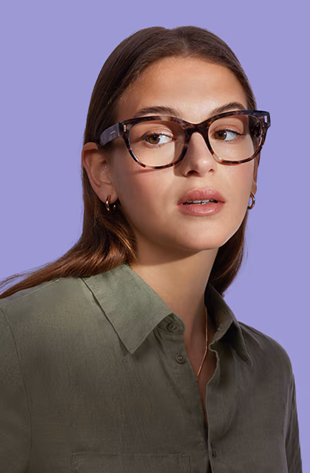 Woman in tortoiseshell glasses looking left, against a purple background