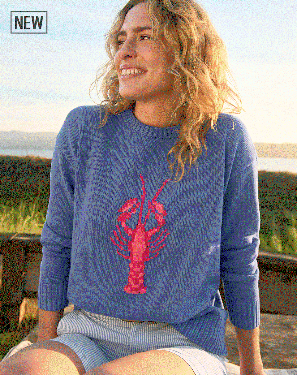 Woman walking on a beach wearing an Original Double L Sweater with a lobster graphic on it.