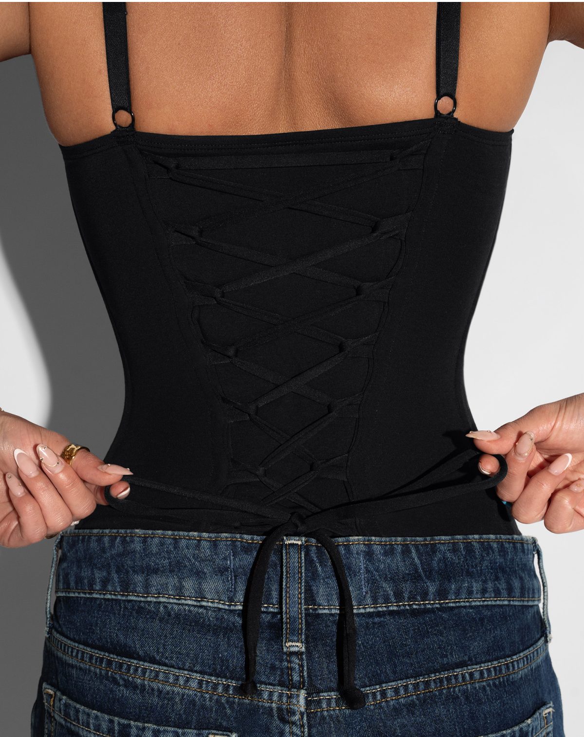 A person tying a black top with a lace-up back, paired with denim shorts.