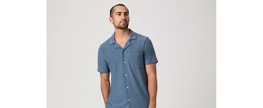 Man wearing a short-sleeve button-up crafted from a micro boucle cotton blend in a mid blue hue, posed in front of a grey backdrop.