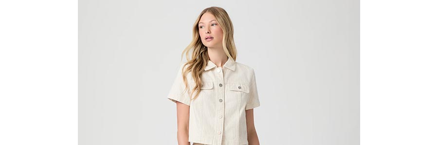 Woman wearing a white striped short sleeve denim jacket in front of a grey backdrop.