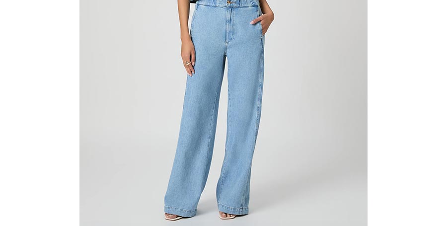 Woman wearing a pair of blue denim high-rise wide leg pants in front of a grey backdrop.
