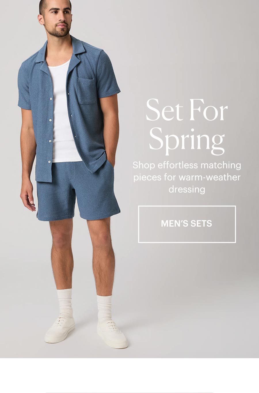 Man wearing a matching blue boucle short sleeve button up and shorts set with a white tee and sneakers in front of a grey backdrop. Set For Spring - Shop effortless matching pieces for warm-weather dressing. Shop men's matching sets.