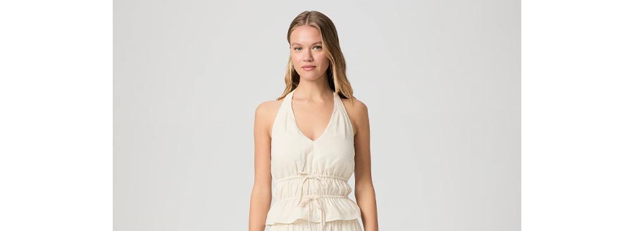 Woman wearing a cream linen ruched halter top in front of a grey backdrop.