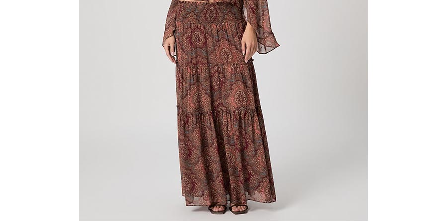 Woman wearing a silk medallion print tiered maxi skirt in front of a grey backdrop.