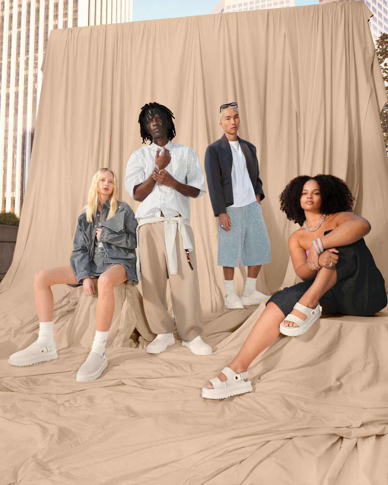 Four individuals in UGG footwear and casual outfits pose outdoors before a draped fabric.
