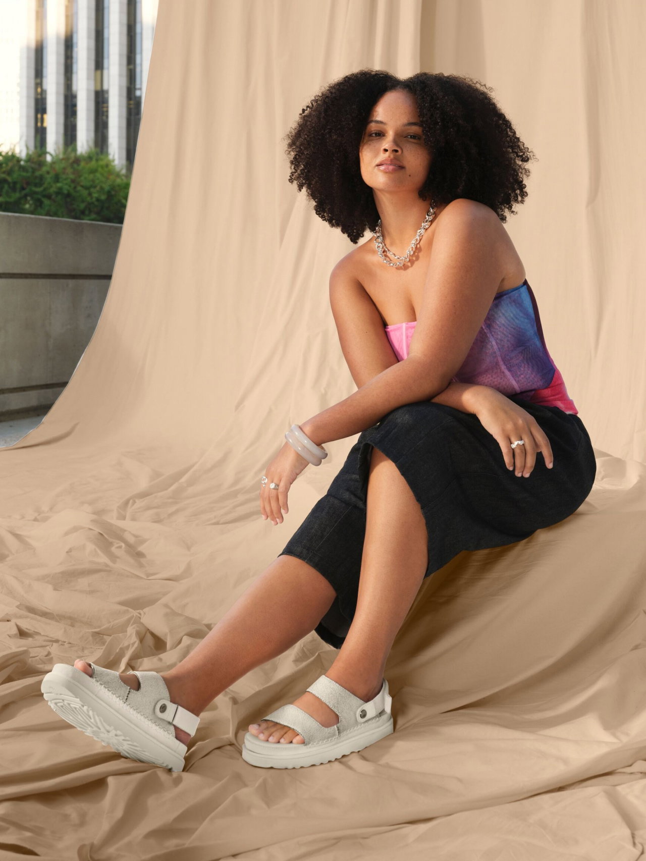 A model in UGG Sandals poses outdoors in front of a draped fabric.