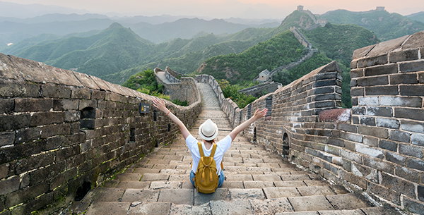 Frau sitzt auf den Treppen der Großen Mauer in China und schaut auf die sich durch die Landschaft schlängelnde Mauer.