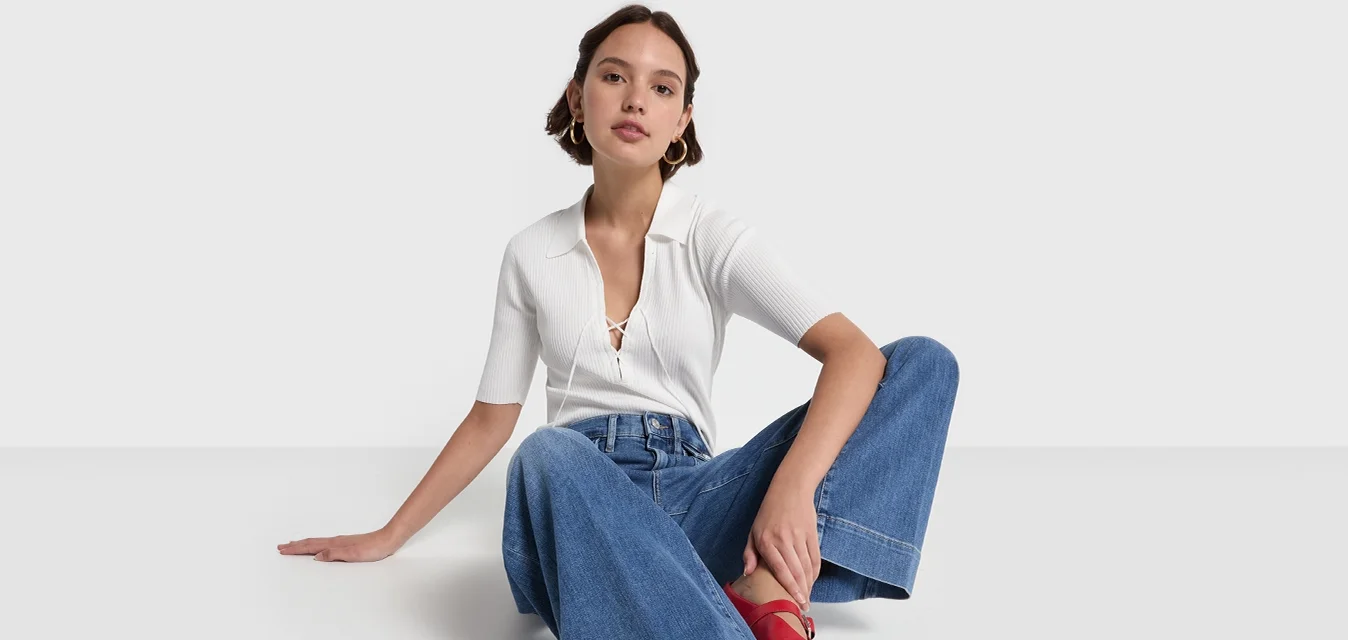 Witte geribbelde blouse met korte mouwen, gecombineerd met lichtblauwe wijde jeans en rode block-heeled schoenen, zittend op een effen achtergrond.