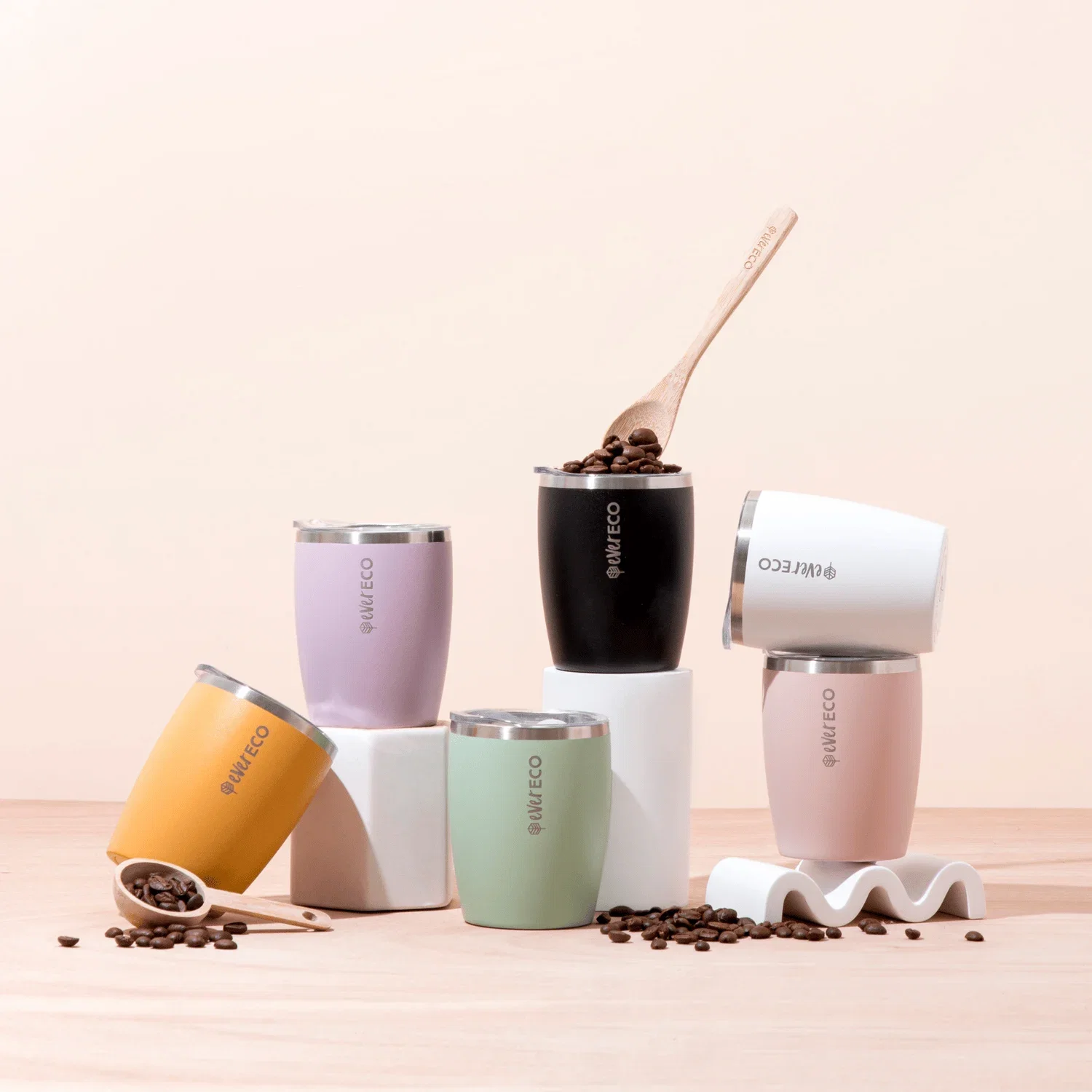 A flat-lay composition features seven colorful tumblers, each with the text 'ever ECO' and a small leaf logo printed on them, arranged on a light pink...