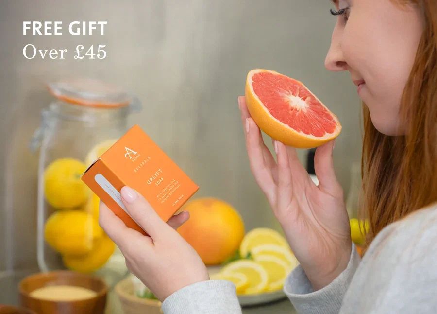 A woman holding a soap bar and smelling a slice of grapefruit