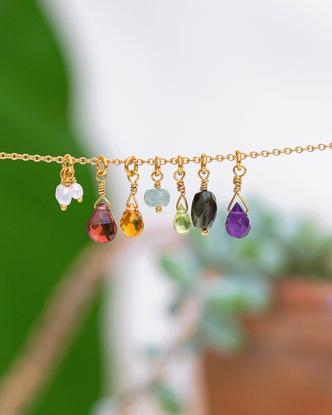 Gold chain with colourful gemstone briolettes including garnet, citrine, peridot, amethyst and pearls, styled against a soft natural background