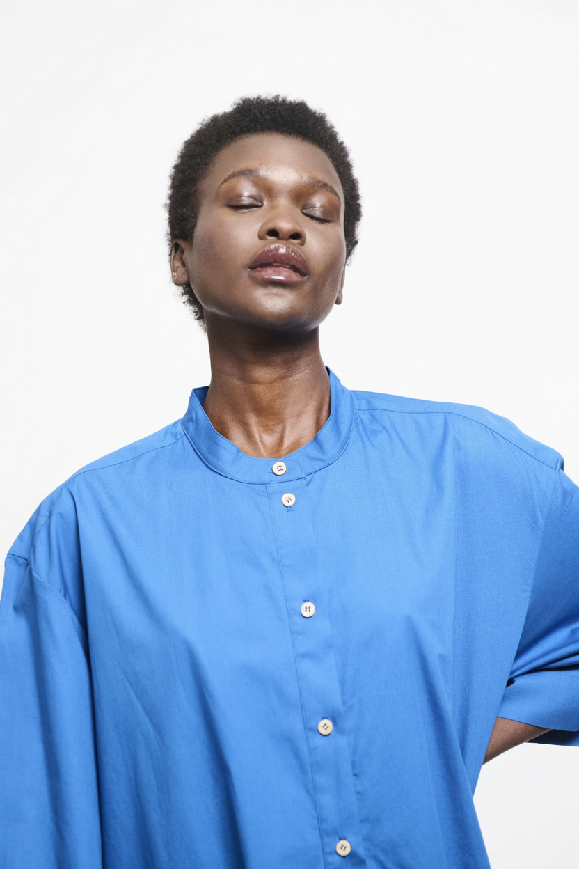 A woman with closed eyes wears a blue button-up shirt.