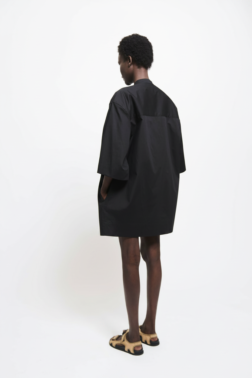 Man in black oversized shirt and tan sandals, viewed from the back.