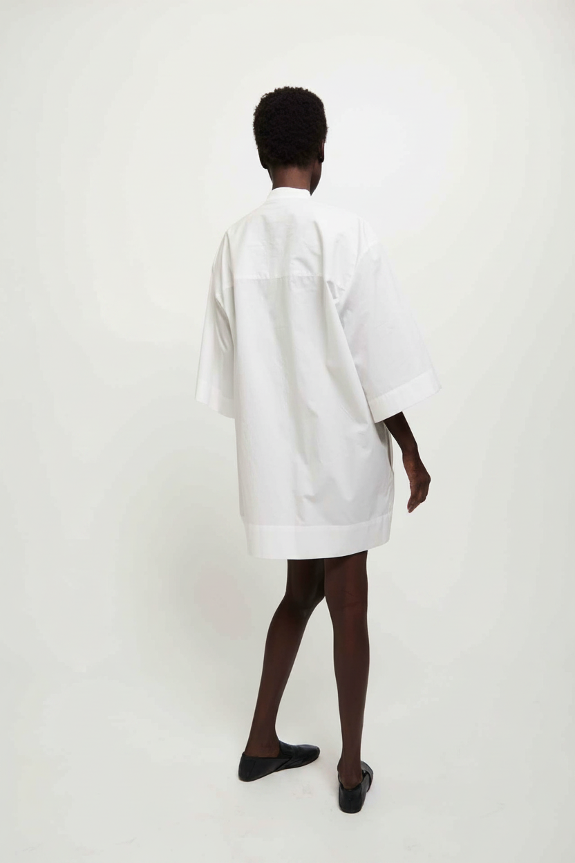 Back view of a person wearing a white oversized shirt dress and black slip-on shoes.