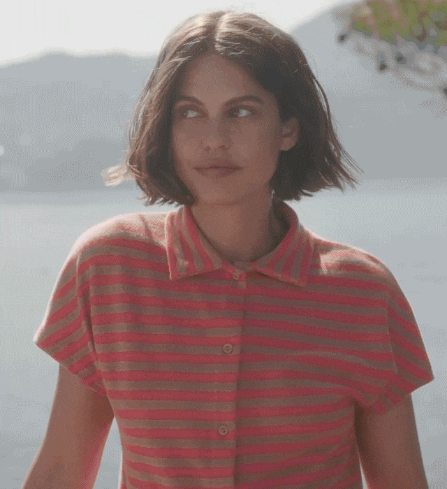 The model is wearing a striped short-sleeve button-down shirt made of terry cloth, a striped terry cloth bustier, and striped terry cloth lounge shorts—all in the color Timeless Taupe and from CALIDA’s Lounge Stripe collection.