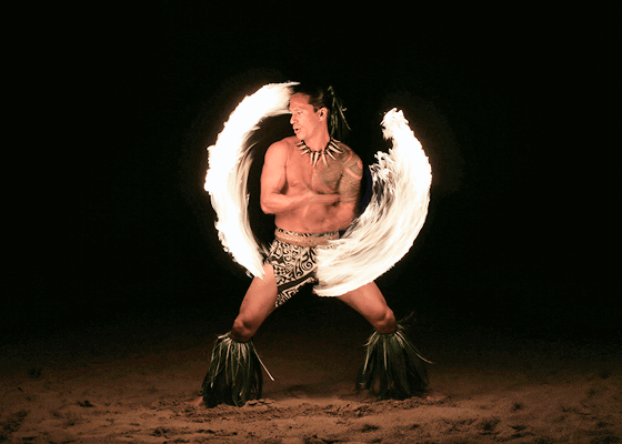 A man dressed in traditional Hawaiian clothing wielding a lit torch in a fire dance