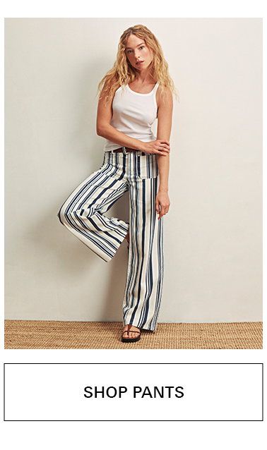 A woman in a white tank top and wide-leg, high-waisted striped pants stands against a plain background, posing with one leg bent. Text below reads "SHOP PANTS.