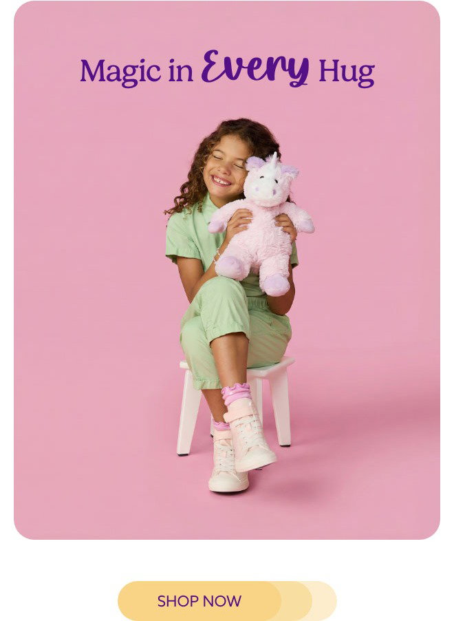 A little girl hugging a Unicorn Warmies on a pink background. Shop Now.